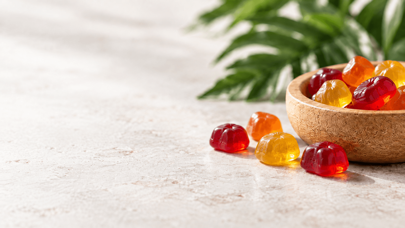 Colorful gummies beside a wooden bowl on a stone tabletop