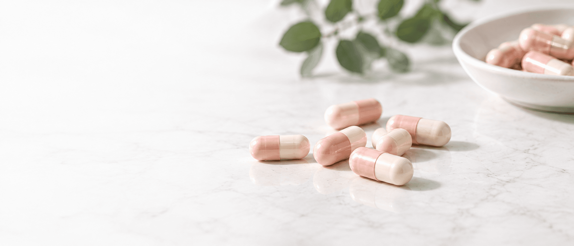 Pink and ivory capsules on a light surface beside a ceramic bowl