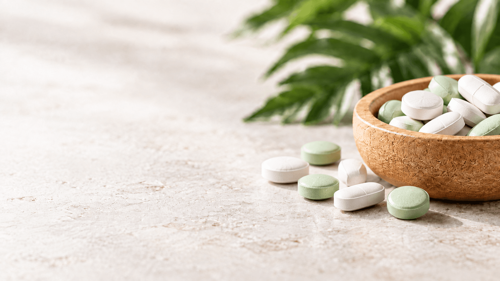 White and pale green supplement tablets in a wooden bowl on a stone tabletop